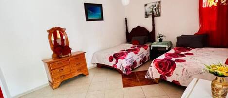 A bedroom with two beds, a wooden dresser, a ceiling fan, and a small table with a plant.