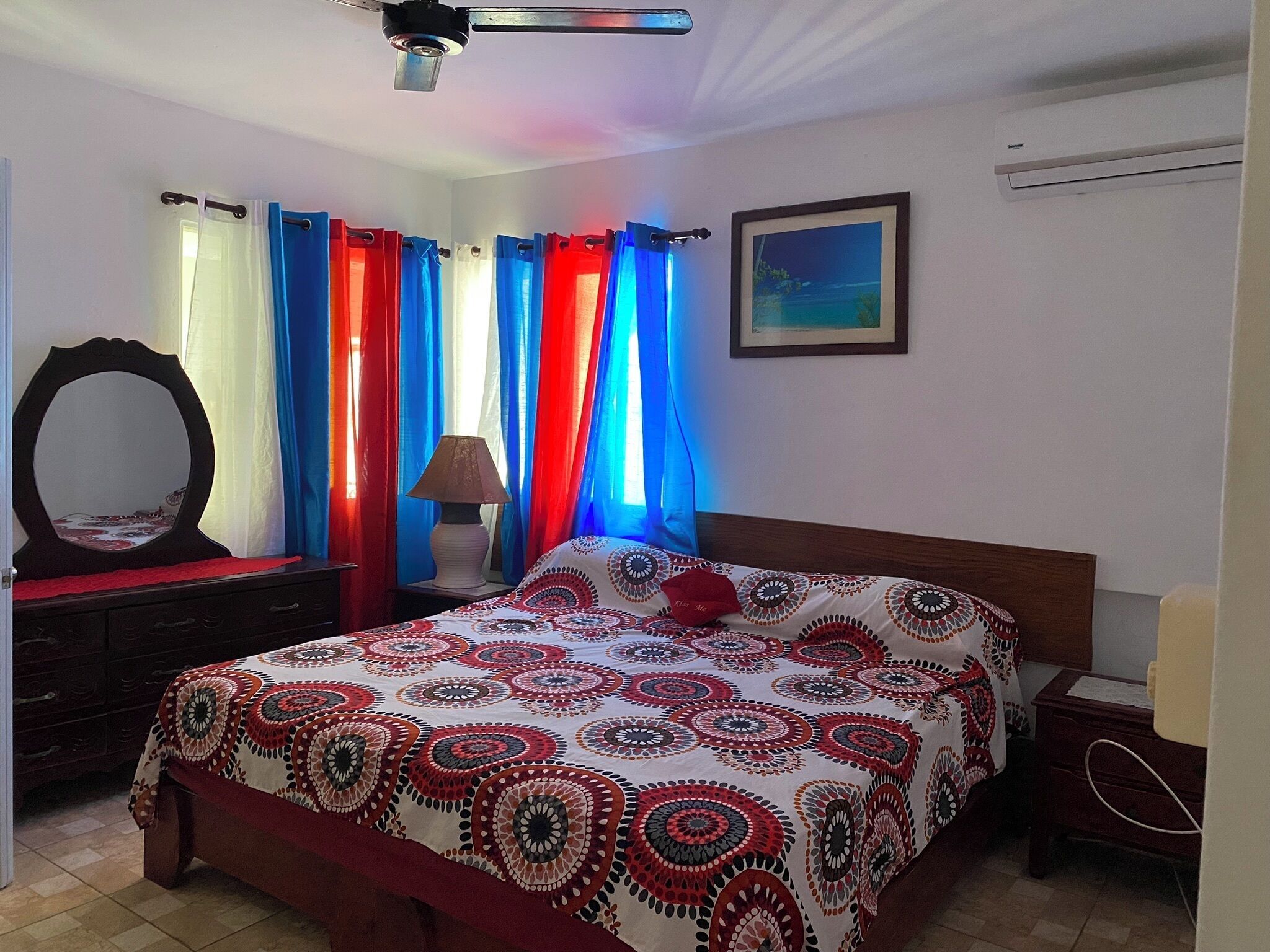 A bedroom with a bed, a dresser, a mirror, curtains, a lamp, and a painting on the wall.
