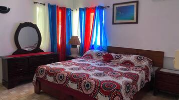 A bedroom with a bed, a dresser, a mirror, curtains, a lamp, and a framed picture on the wall.