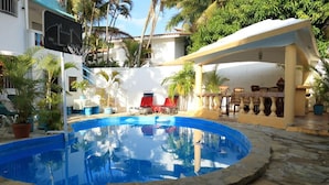 A swimming pool with a stone border, surrounded by potted plants and outdoor furniture. - Villa Antonia 16 (Sosúa)