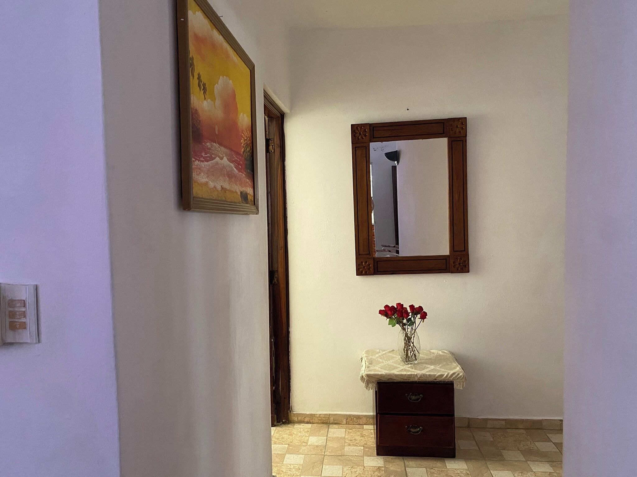 Un pasillo con un cuadro, un espejo y una pequeña mesa con un jarrón de flores.