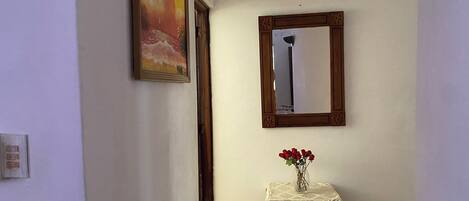 A hallway with a painting, a mirror, and a small table with a vase of flowers.
