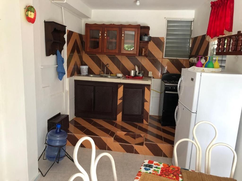 Uma cozinha compacta com piso em padrão herringbone, armários de madeira, geladeira branca e dispenser de água azul.