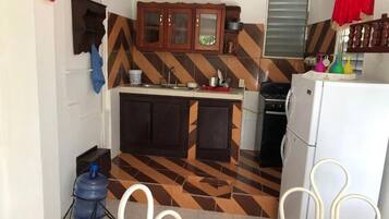Uma cozinha compacta com piso em padrão herringbone, armários de madeira, geladeira branca e dispenser de água azul.