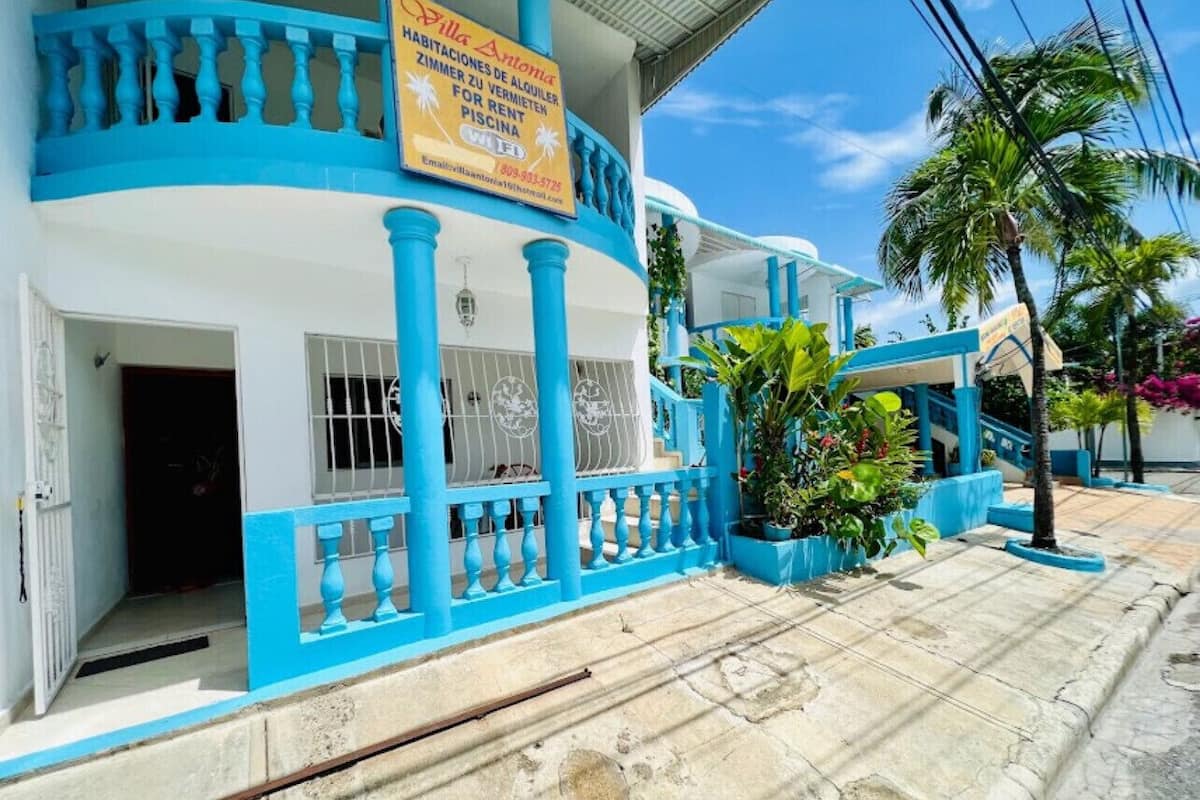 A two-story building with a blue and white facade, featuring a balcony with blue railings and a sign advertising rental apartments.