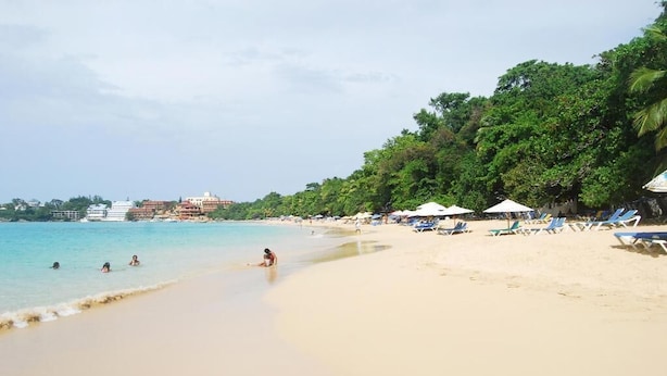 A beach with clear turquoise water, a sandy shore, and a row of beach umbrellas and lounge chairs. - Villa Antonia 16 (Sosúa)