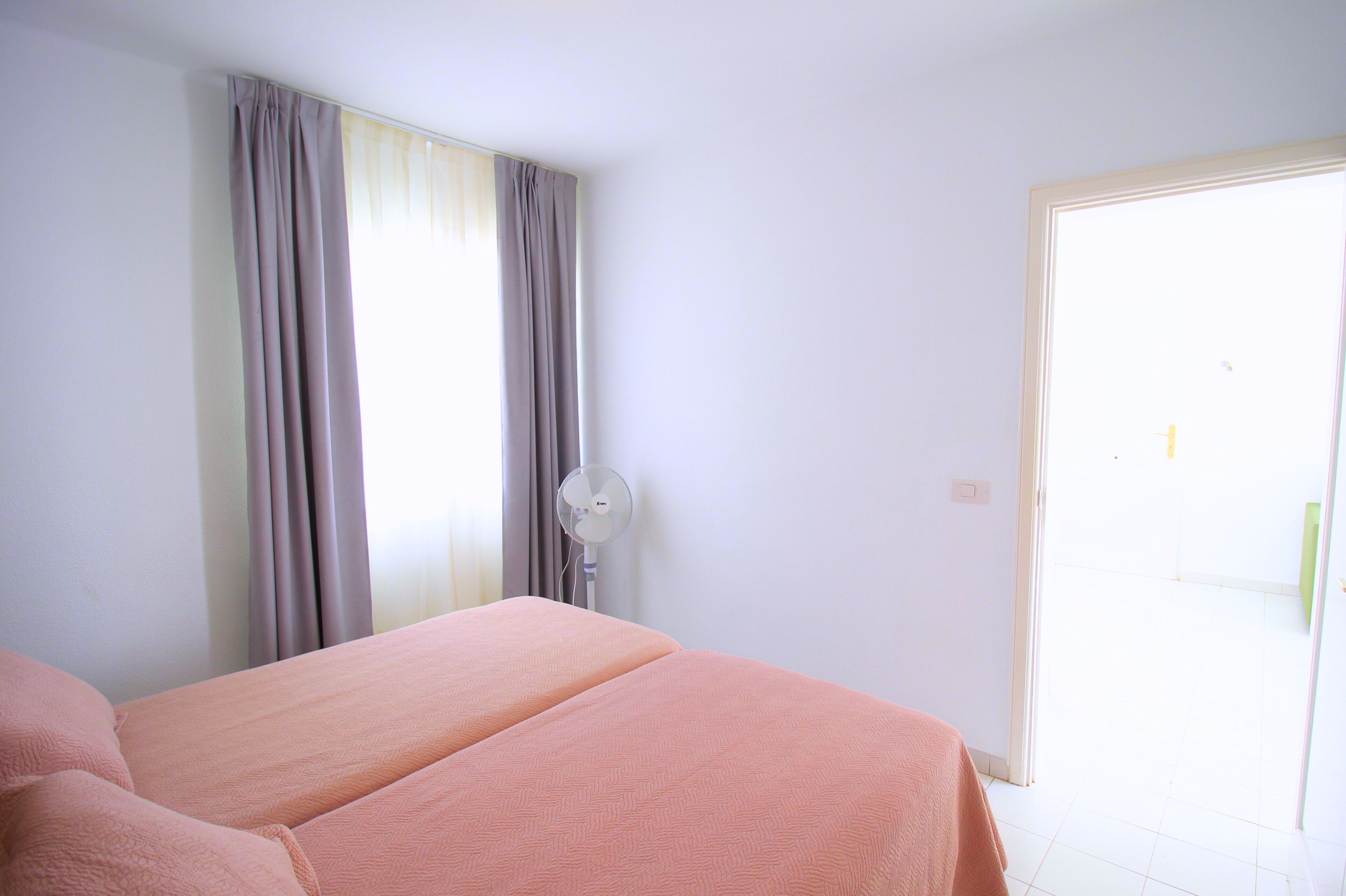Un dormitorio con cama, cortinas, ventilador y puerta que da a un espacio exterior.