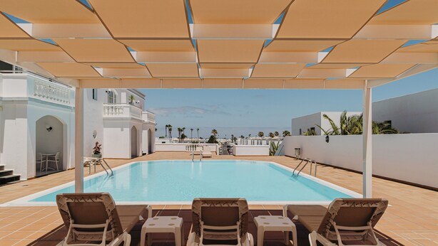A pool area with lounge chairs, a pool, and a view of the sea.