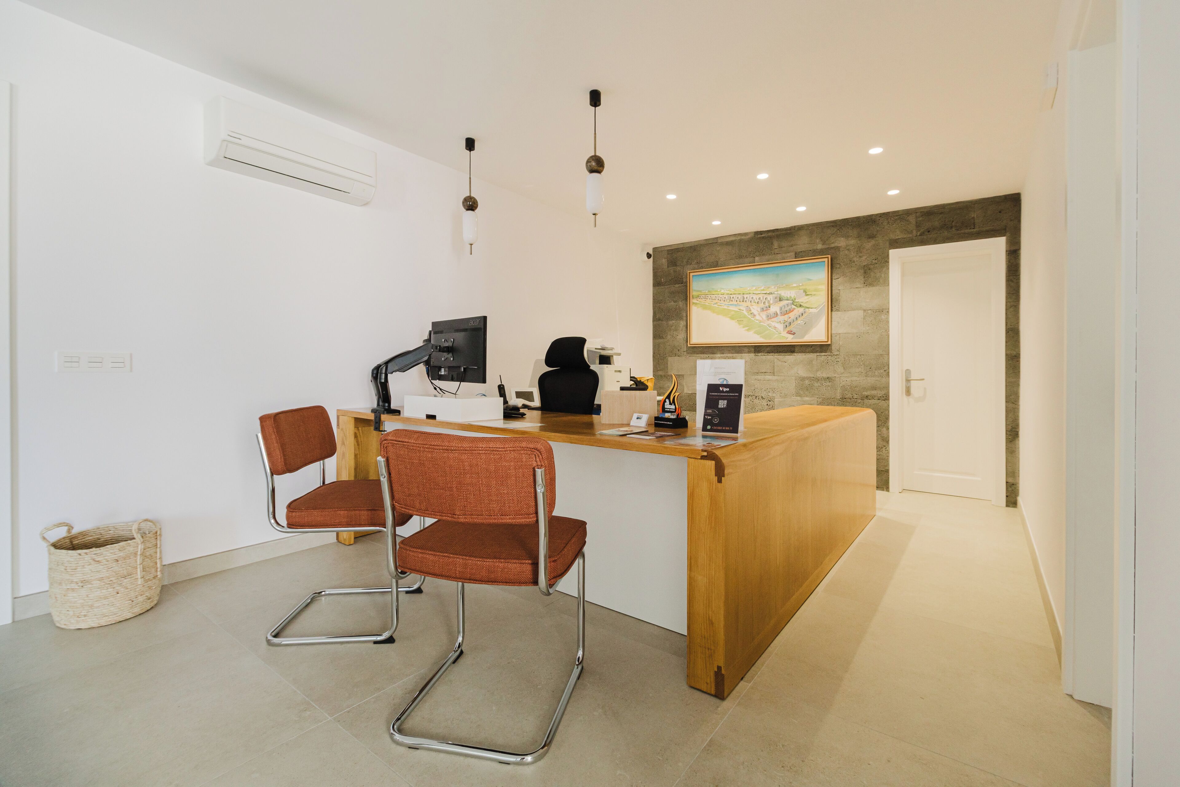 Un mostrador de recepción con una computadora, una silla y un cuadro en la pared.