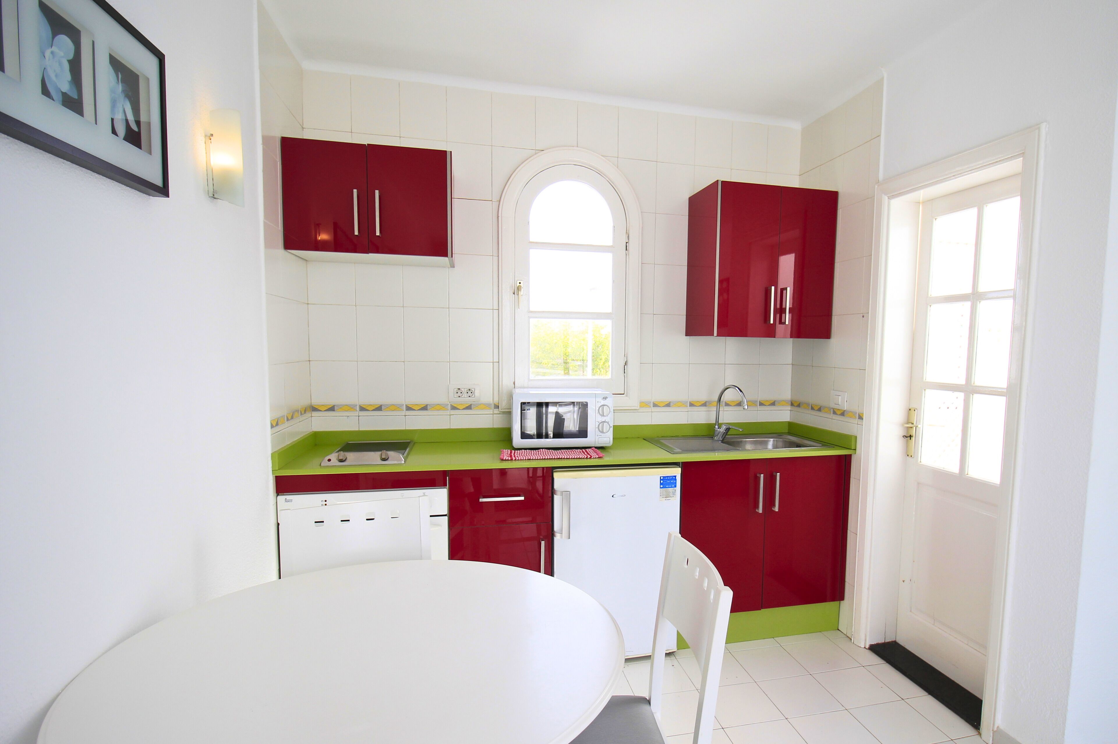 A compact kitchen with white cabinets, a red countertop, a white sink, and a small refrigerator.