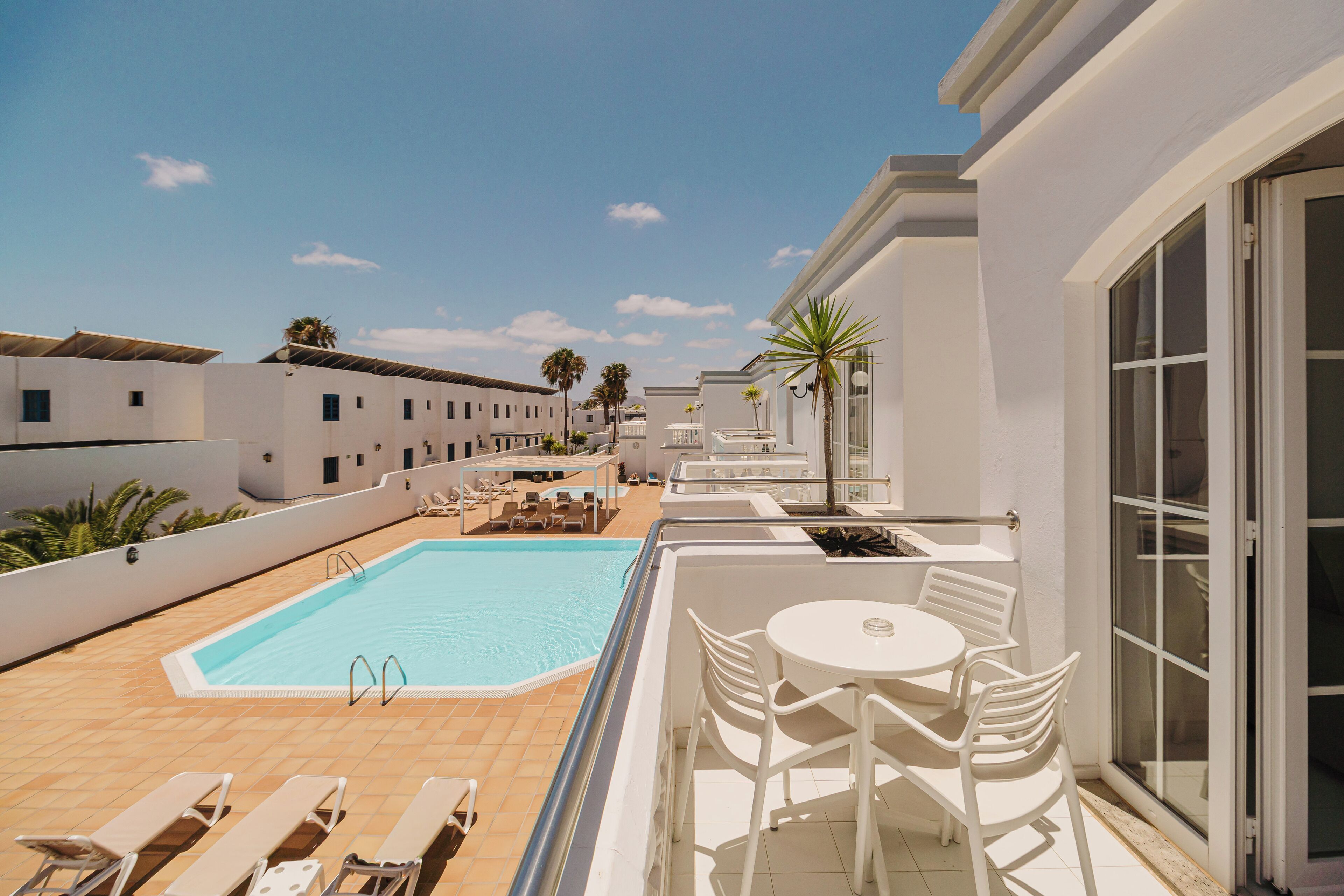 Un área de piscina en la azotea con sillones, una mesa y una piscina.