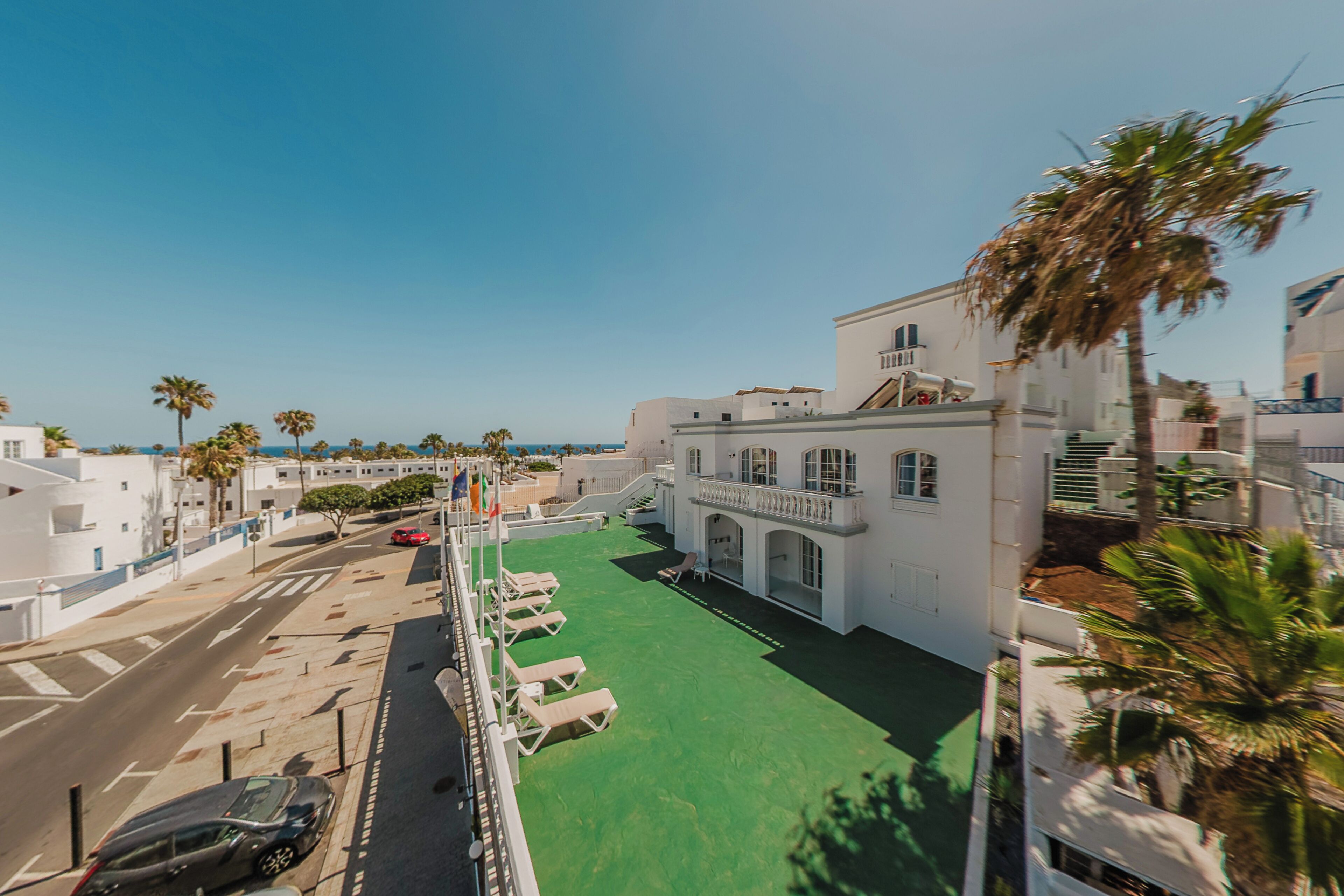 A hotel with a green courtyard, palm trees, and a view of the sea.