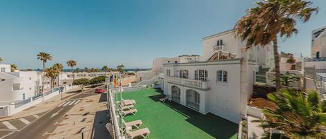 A hotel with a green courtyard, palm trees, and a view of the sea.