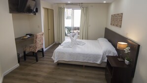 Ein Hotelzimmer mit einem Bett, einem Schreibtisch, einem Sessel, einem an der Wand montierten Fernseher und einer Topfpflanze.