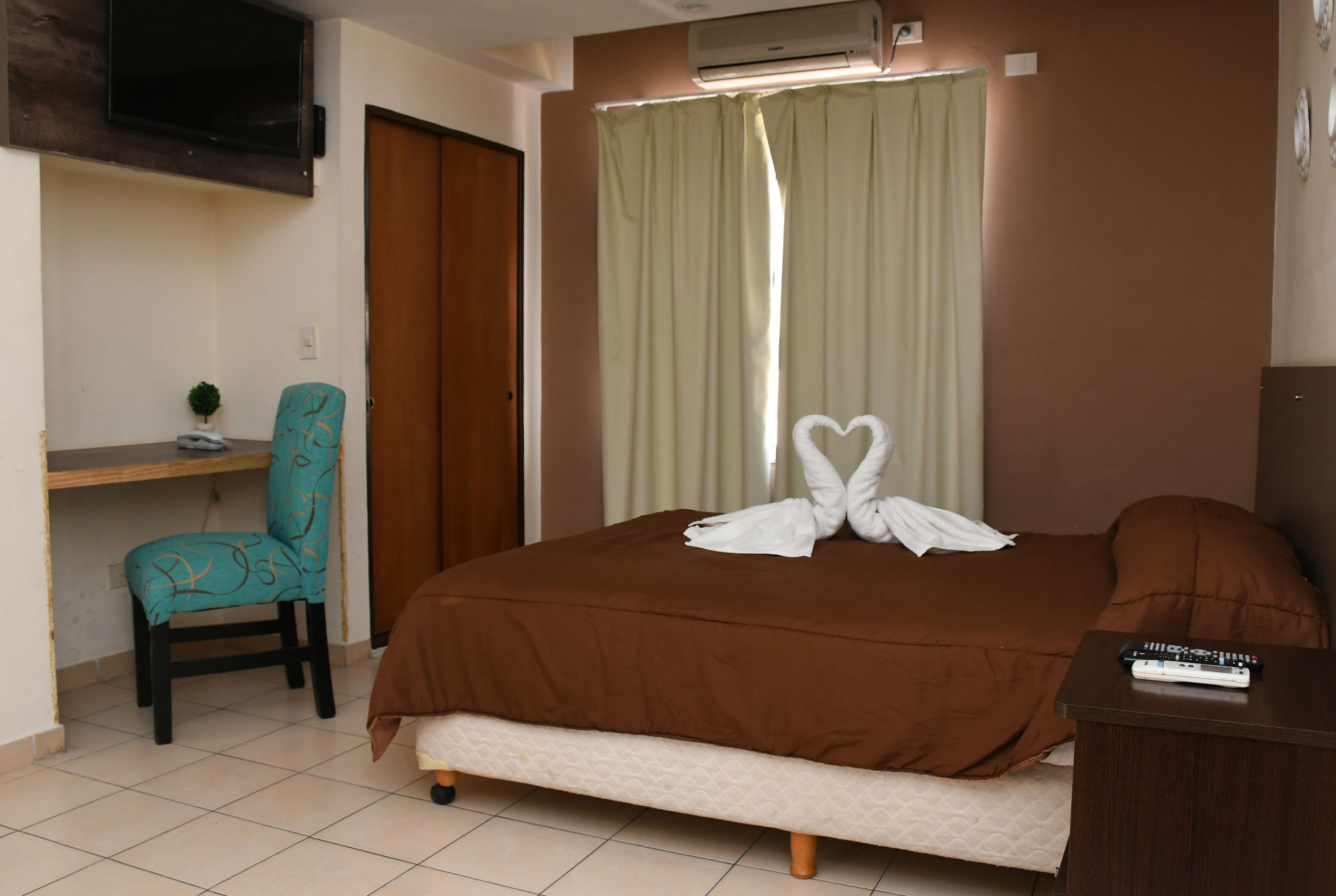 A hotel room with a bed, a desk, a chair, and a television.