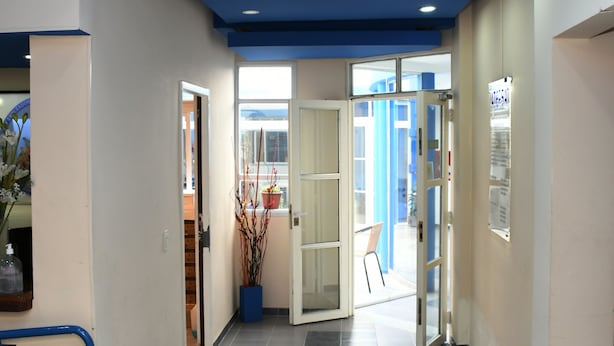 Ein Flur mit blauer Decke, Fliesenboden und Glastüren zu einem weiteren Raum.