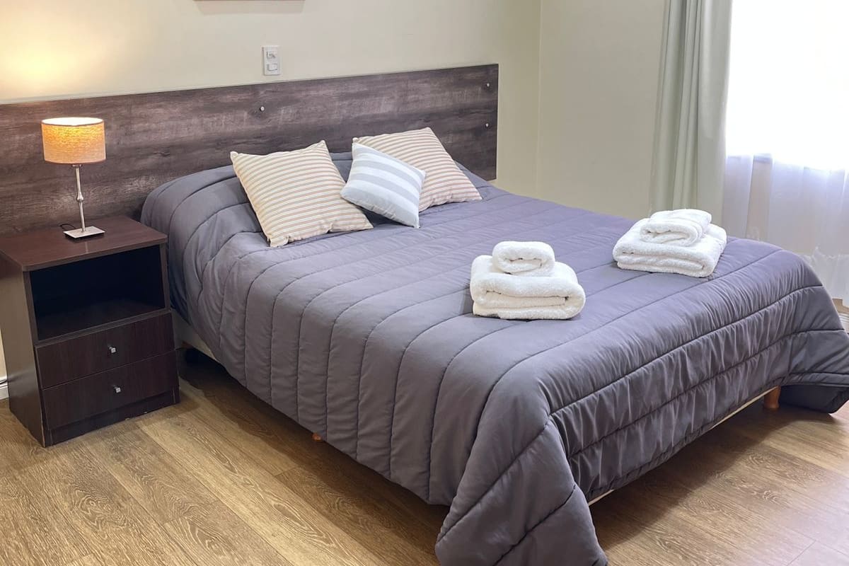 A neatly made bed with a dark grey duvet, two pillows, and two folded towels.
