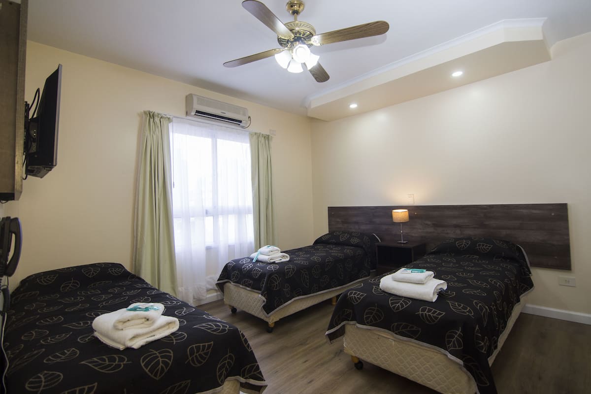 A hotel room with two beds, a ceiling fan, an air conditioning unit, and a window with curtains.