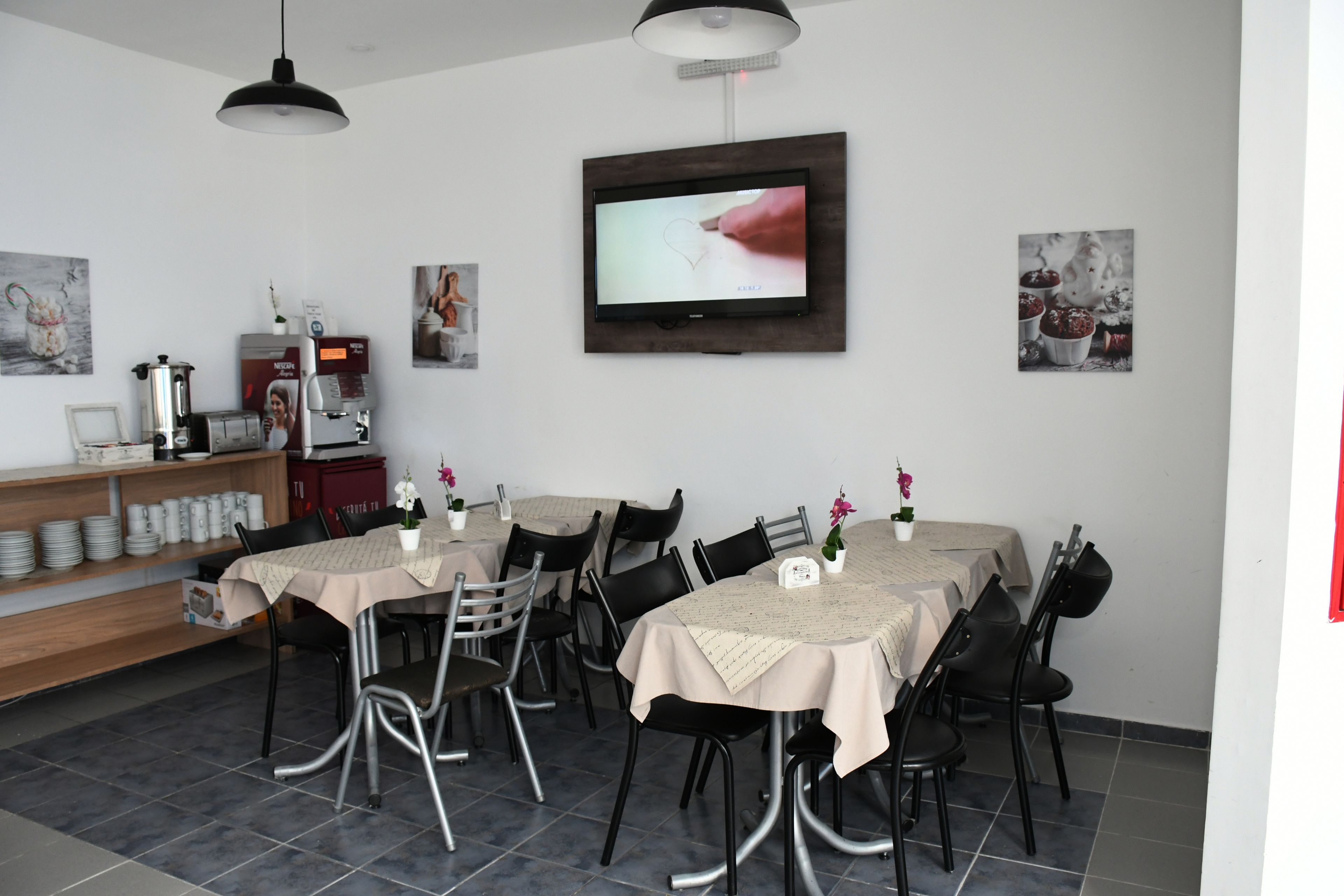 A dining area with a TV mounted on the wall, a coffee machine, and a shelf with plates and cups.