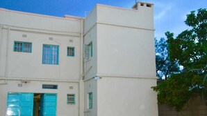 A two-story building with a flat facade, large windows with blue frames, and a pair of open blue doors at the ground level. - Quest Resort (Nakuru)