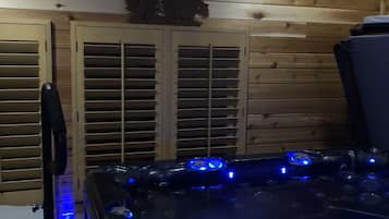 Ein Holzblockhaus-Interieur mit Whirlpool, der blaue LED-Leuchten, Holzläden und eine Bär-Silhouette an der Wand zeigt.