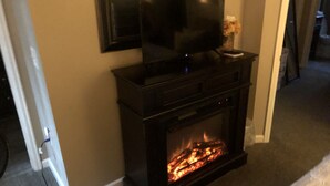 A living room with a fireplace, a television mounted above it, and a vase with flowers on the mantel. - Denver Blue Bear Romantic Spa Getaway: Private 1 BR Apartment with NEW Spa Room (Denver)