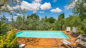Um deck de madeira com piscina, rodeado por árvores e vegetação.