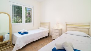 Una camera d'albergo con due letti singoli, un comodino con una lampada, uno specchio e una finestra vista verde.