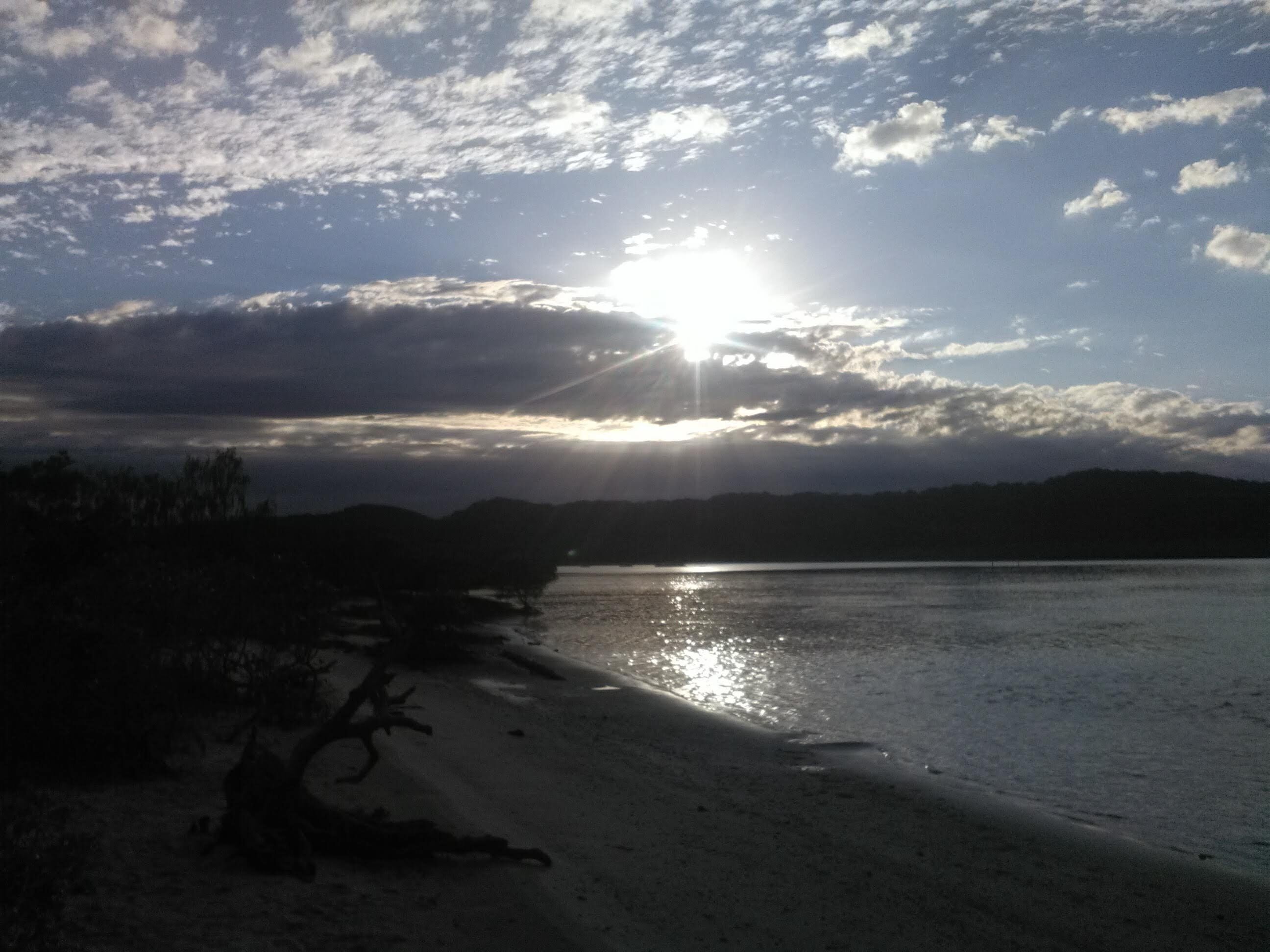 A beach with a sunset, calm water, and distant mountains.
