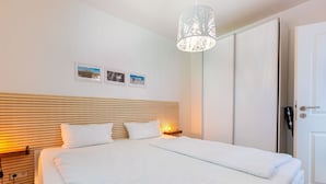 A neatly made bed with white linens, a wooden slatted headboard, and a pendant light fixture. - Apartment 1 Küstenkind (ID 391) (Sankt Peter-Ording)