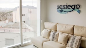 Ein modernes Wohnzimmer mit einem beigen Sofa und einem großen Fenster mit Blick auf eine Stadtlandschaft.
