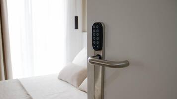 Ein modernes Hotelzimmer mit elektronischer Türverriegelung an der Wand und einem Bett mit weißer Bettwäsche.