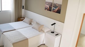 Ein Hotelzimmer mit zwei Betten, einem Nachttisch mit Lampe sowie einem an der Wand hängenden Kunstwerk.