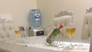 Et spisebord med en dekorativ metalkulptur, to glas vin og en vanddispenser i baggrunden.