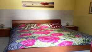 A bed with a floral bedspread, two pillows, a nightstand with a lamp, and a painting on the wall. - Beautiful house - fiumefreddo (fiumofreddo)
