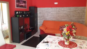 A room with a red wall, a grey textured partition, an orange sofa, a dining table with a floral tablecloth, and a vase with flowers. - Beautiful house - fiumefreddo (fiumofreddo)