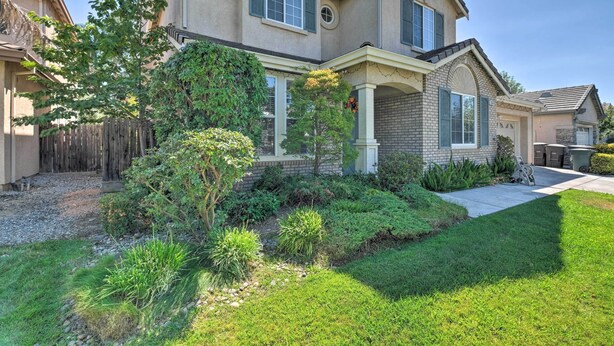 A two-story house with a brick facade, a covered porch, and a well-maintained front yard with various plants and a gravel path. - Family-Friendly Tracy House with Patio & Grill! (Tracy)