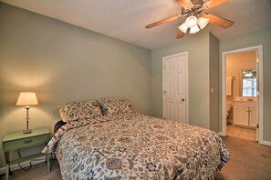 Un dormitorio con una cama, una mesita de noche con lámpara, un ventilador de techo y una puerta que da a un baño.