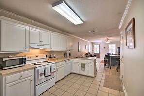Una cocina con armarios blancos, microondas, estufa y ventilador de techo.