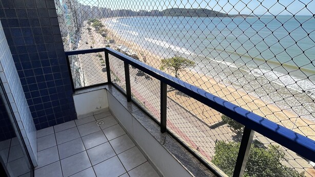 Ein Balkon mit einem Maschendrahtzaun, der Blick auf Strand und Meer bietet.
