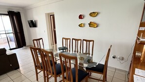 Ein Essbereich mit einem runden Tisch, sechs Holzsesseln und einem an der Wand montierten Fernseher.