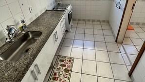 Eine Küche mit weiß gefliesten Wänden, einer Granitarbeitsplatte, einer Spüle, einem Herd und einem Fenster mit Blick nach außen.