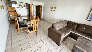 Ein Wohnzimmer mit einem braunen Sofa, einem Glastisch mit Holzstühlen und einem durchgehenden Durchgang zur Küche.