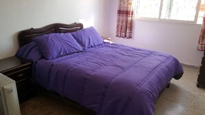 Une chambre à coucher avec un lit, une table de chevet, un radiateur et une fenêtre avec des rideaux.
