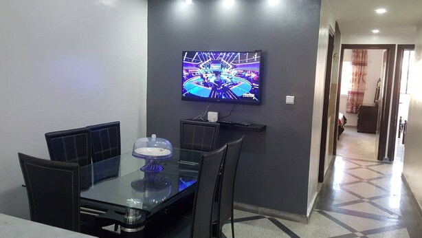 Un coin repas avec une table en verre, des chaises noires et un téléviseur fixé au mur.