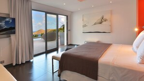 A modern hotel room with a large bed, a flat-screen TV, a sliding glass door to a balcony, and a painting on the wall.