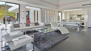A modern living room with a glass coffee table, white sofas, and a large window overlooking a scenic landscape.