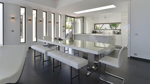 A modern kitchen with a central island, white bar stools, and a long dining table.