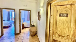 Ein Flur, der zu einem Waschraum mit einer Holztür und einem gefliesten Boden führt, nebenan ist ein Bett zu sehen.