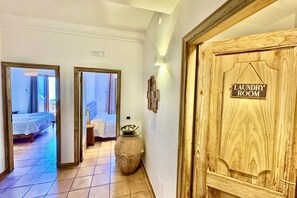 Un pasillo que conduce a un lavadero con puerta de madera, suelo de baldosas y una cama en la habitación contigua.